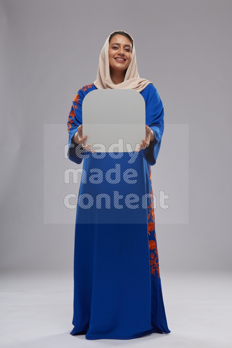 A Saudi woman standing wearing Jalabeya holding a social media sign