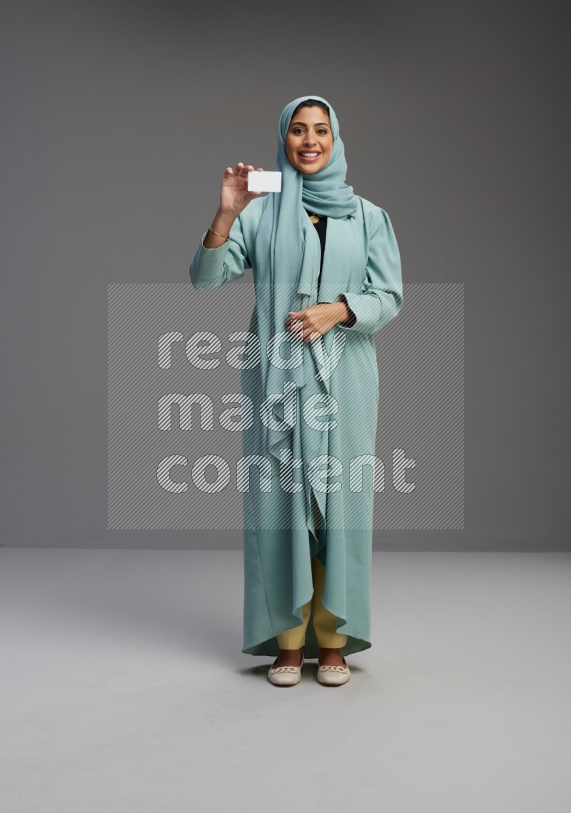 Saudi Woman wearing Abaya standing holding ATM card on Gray background
