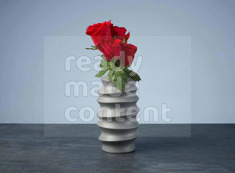 An arrangement of vivid red roses in a grey spiral vase on black marble background