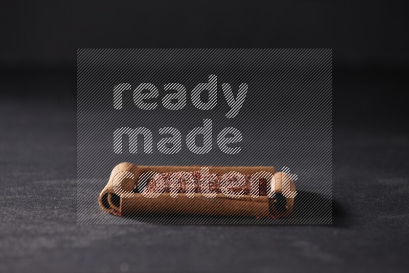 أربعة من أعواد القرفة مكونة شكل مربع بداخلها حب الرشاد علي خلفية سوداء