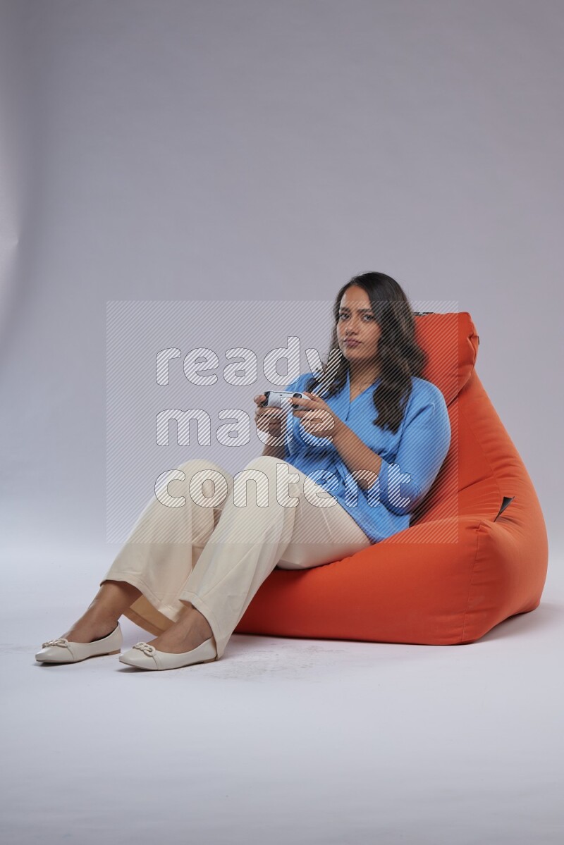 A woman sitting on an orange beanbag and gaming with joystick