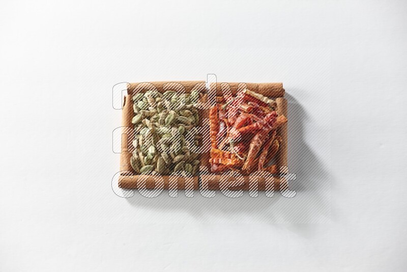 مربعان من أعواد القرفة ممتلئان بحبوب الهيل والفلفل الحار المجفف علي خلفية بيضاء