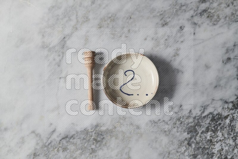Multicolored pottery bowl with wooden honey dipper on the side on grey marble background