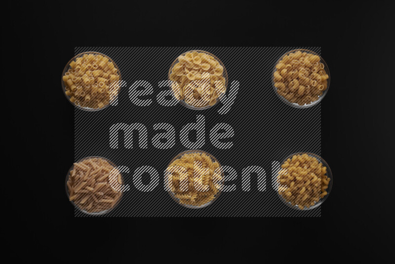 Different pasta types in 6 glass bowls on black background