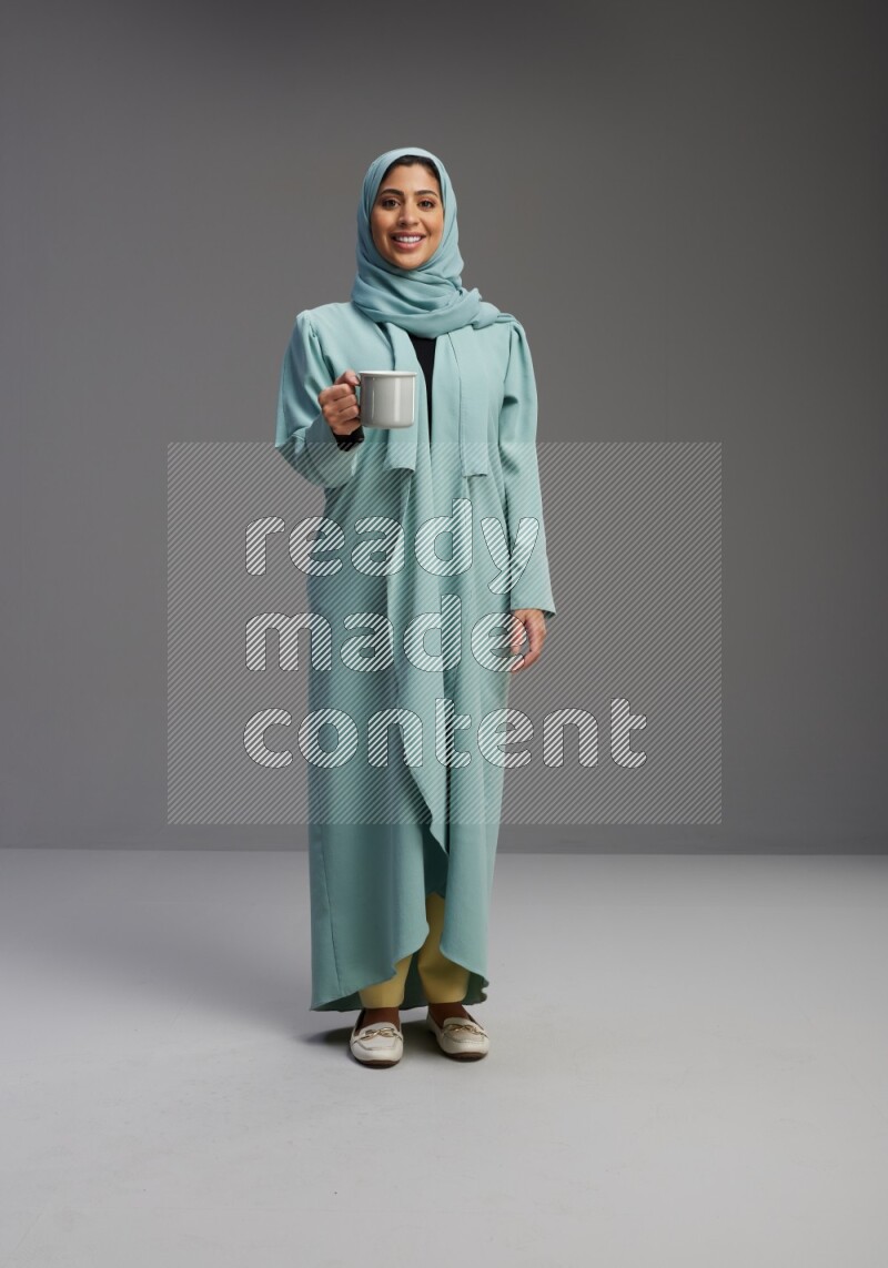 Saudi Woman wearing Abaya standing  holding a mug on Gray background
