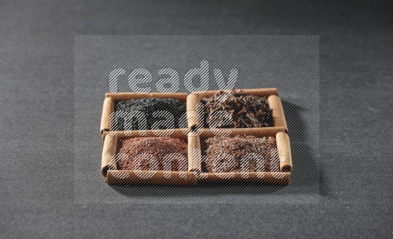 4 squares of cinnamon sticks full of black seeds, garden cress, flaxseeds and cloves on black flooring