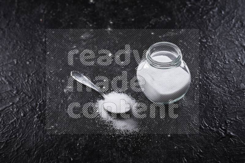 A glass jar full of fine table salt on black background