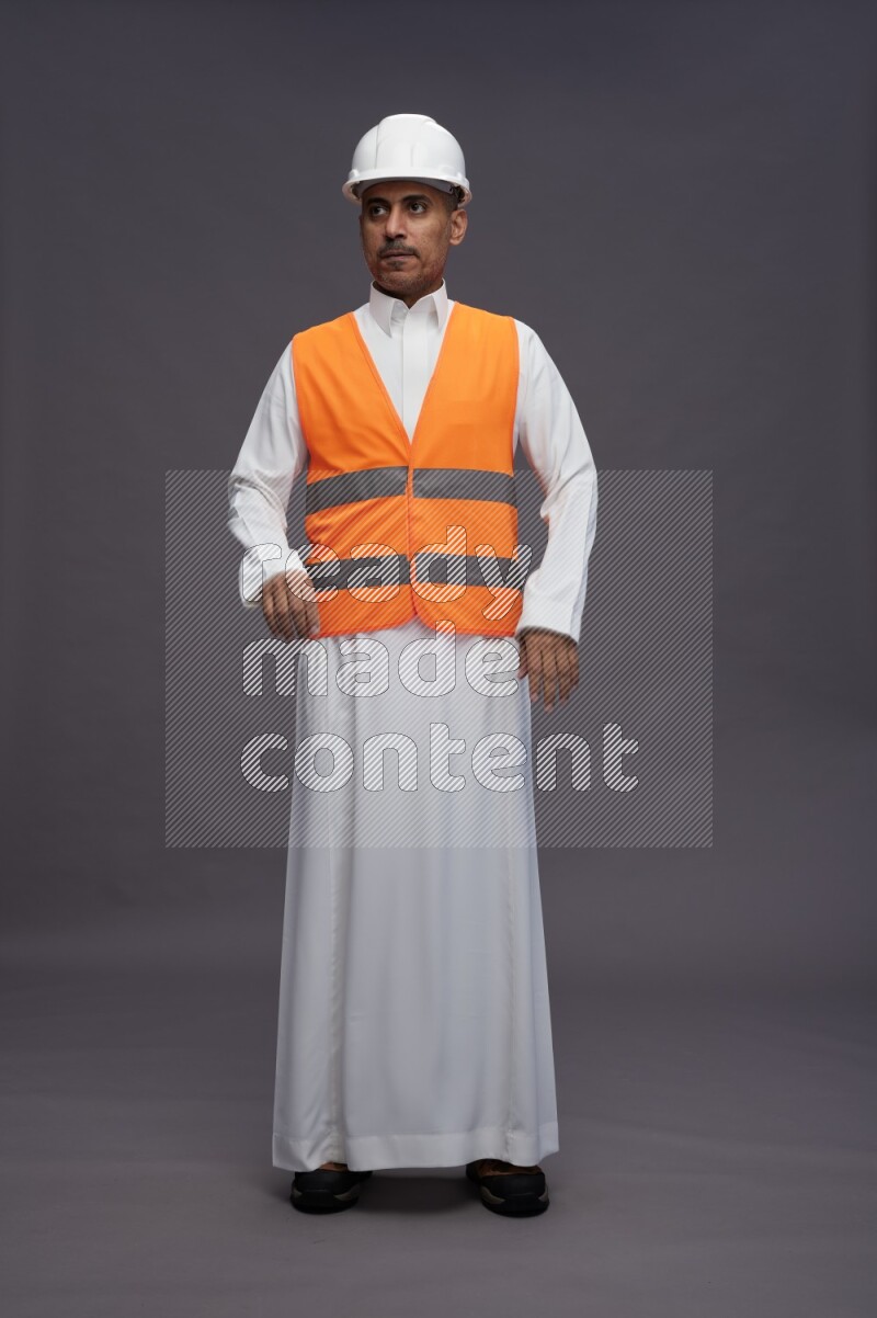 Saudi man wearing thob with engineer vest standing interacting with the camera on gray background