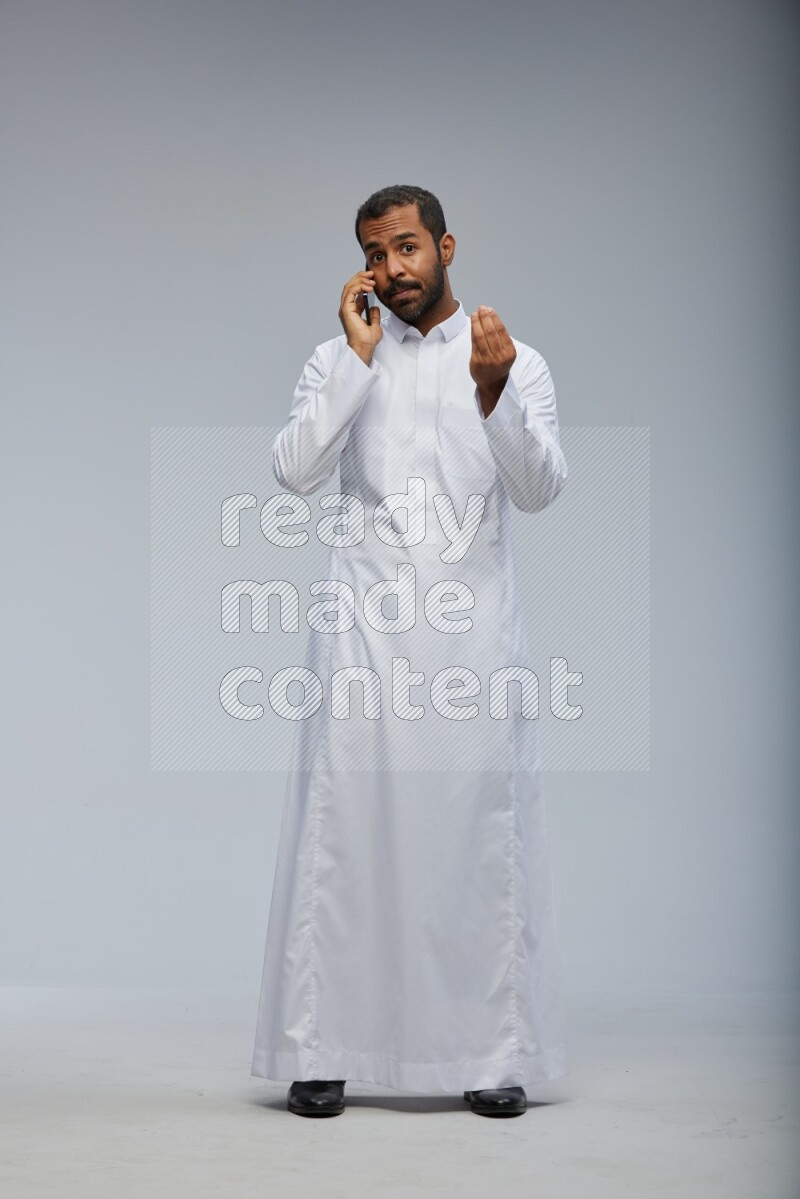 Saudi man wearing Thob standing talking on phone on Gray background