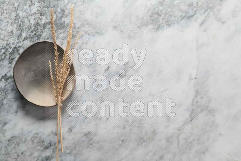 Wheat stalks on multicolored pottery plate on grey marble background