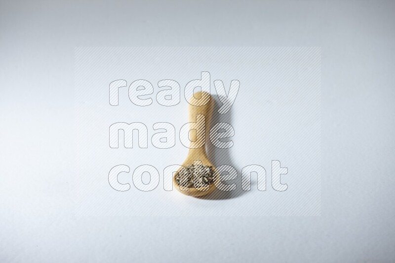 A wooden spoon full of cumin seeds on a white flooring