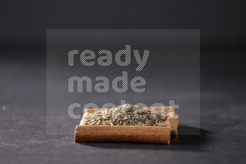 أربعة من أعواد القرفة مكونة شكل مربع بداخلها حبوب الكمون علي خلفية سوداء