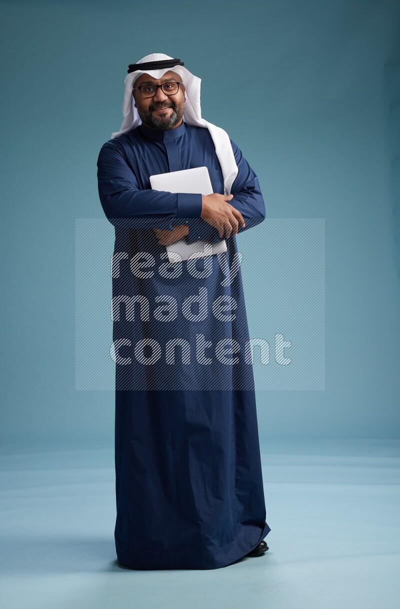 Saudi Man with shimag Standing working on laptop on blue background