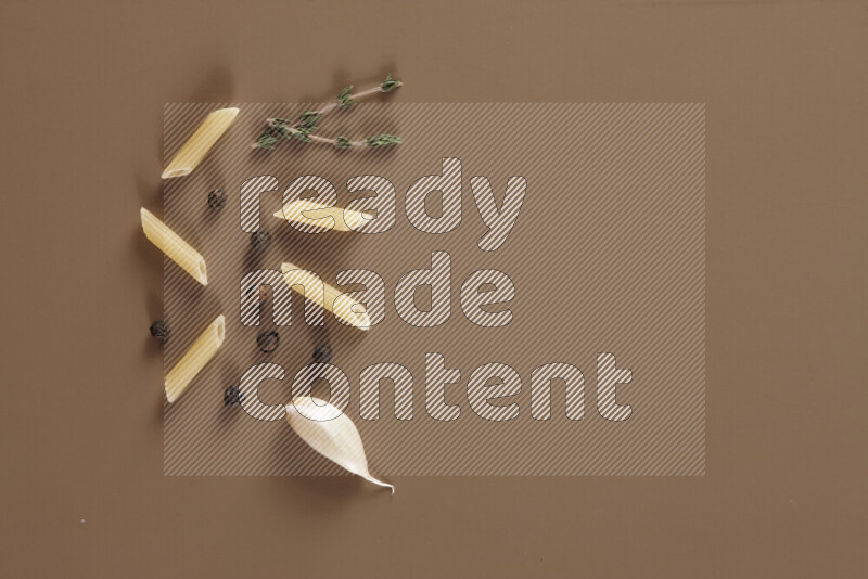 Raw pasta with different ingredients such as cherry tomatoes, garlic, onions, red chilis, black pepper, white pepper, bay laurel leaves, rosemary and cardamom on beige background