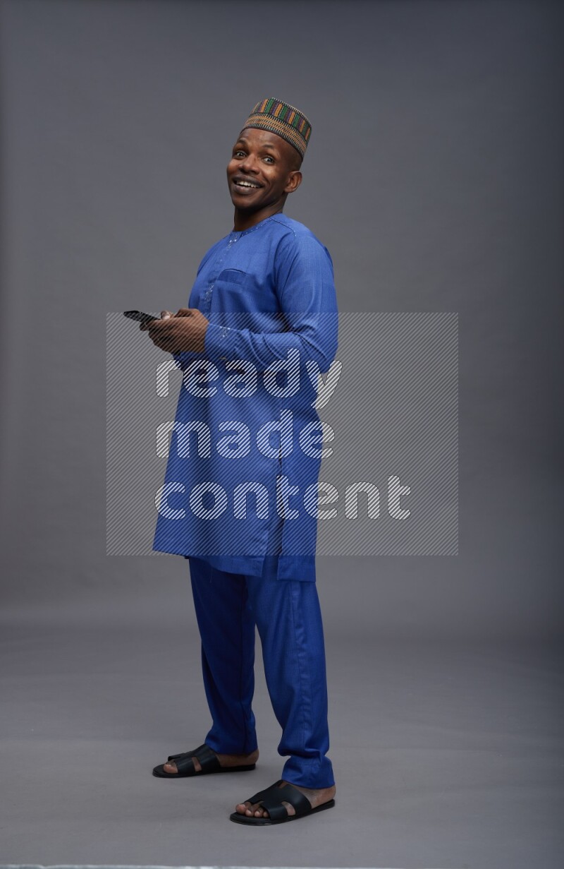 Man wearing Nigerian outfit standing texting on phone on gray background