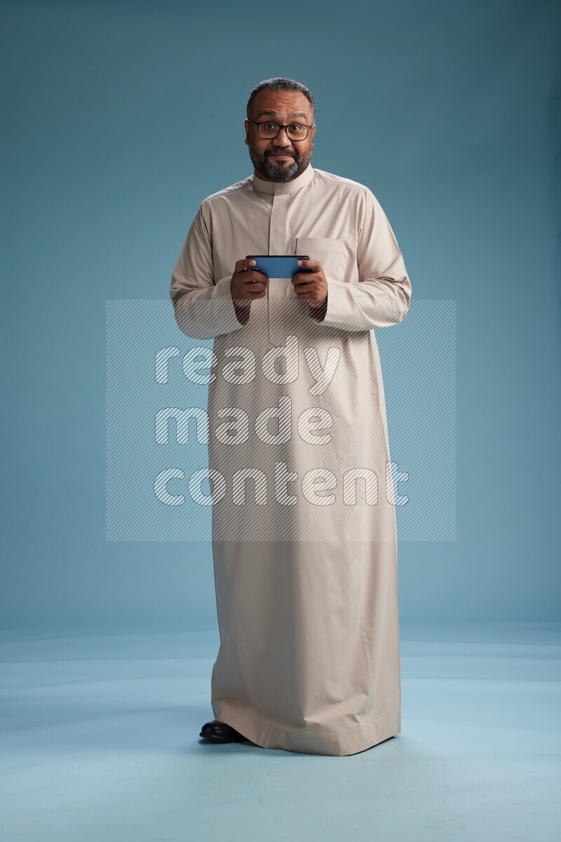 Saudi Man without shimag Standing texting on phone on blue background