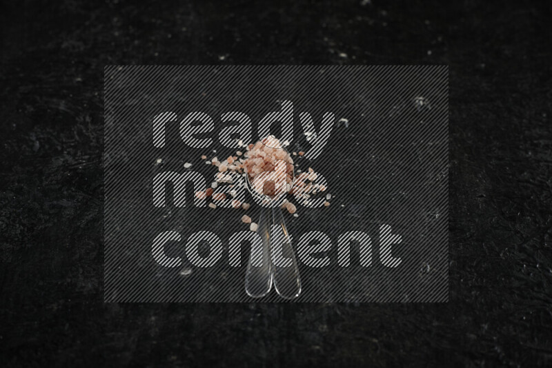 2 metal spoons filled with pink himalayan salt on black background