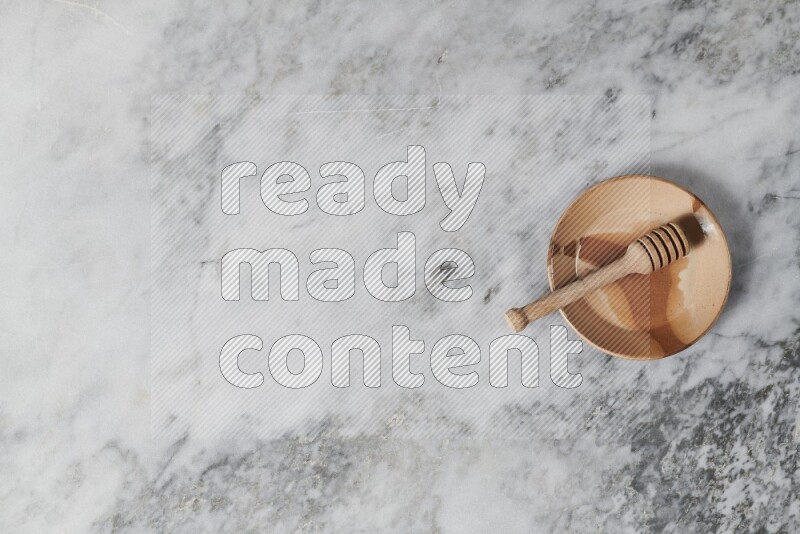Multicolored pottery plate with wooden honey dipper in it on grey marble background