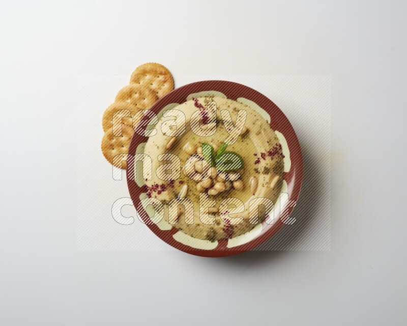 Hummus in a traditional plate garnished with zaatar & sumak on a white background