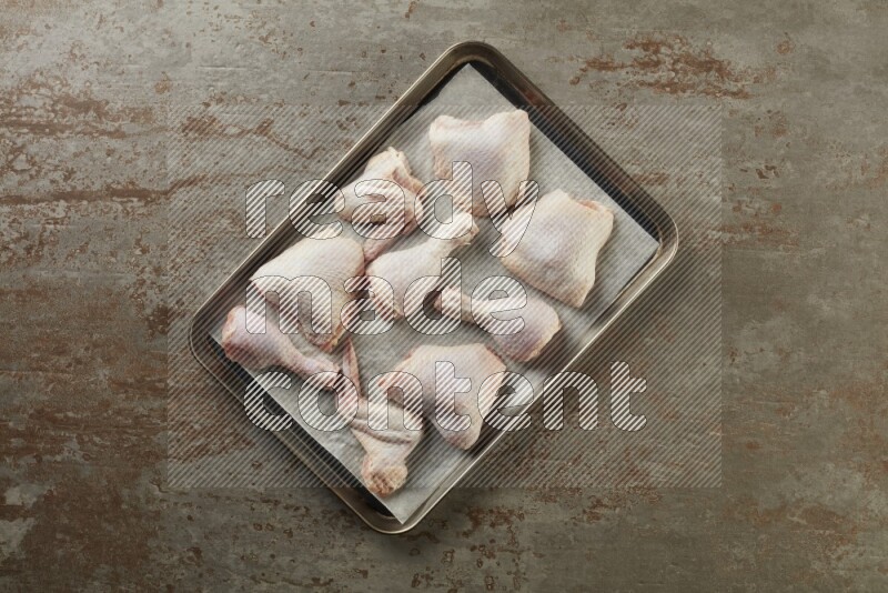 Mixed fresh chicken pieces in an oven tray on a textured rustic background