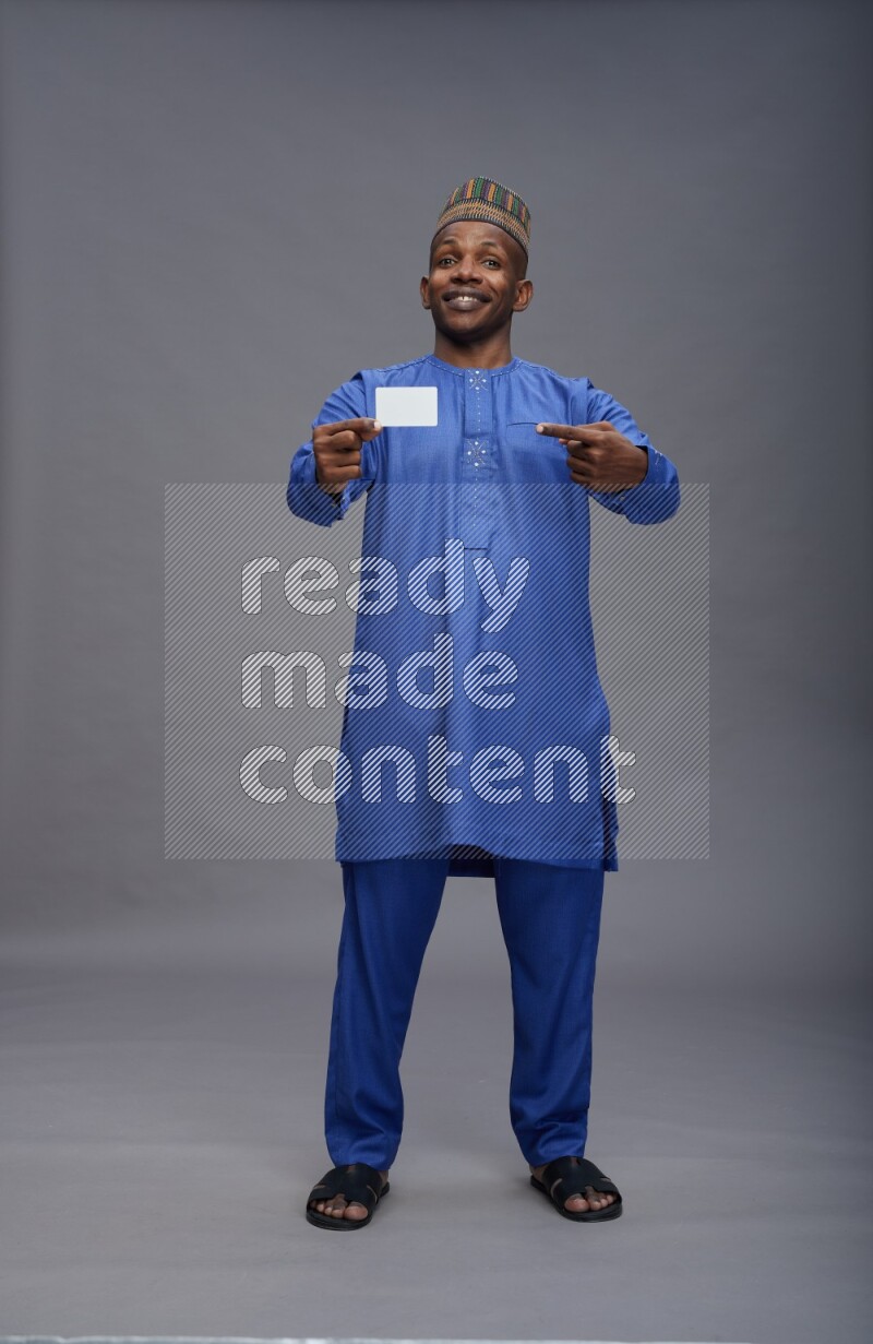 Man wearing Nigerian outfit standing holding ATM card on gray background