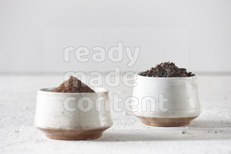2 Beige ceramic bowls, one full of cloves and the other full of powder on textured white flooring