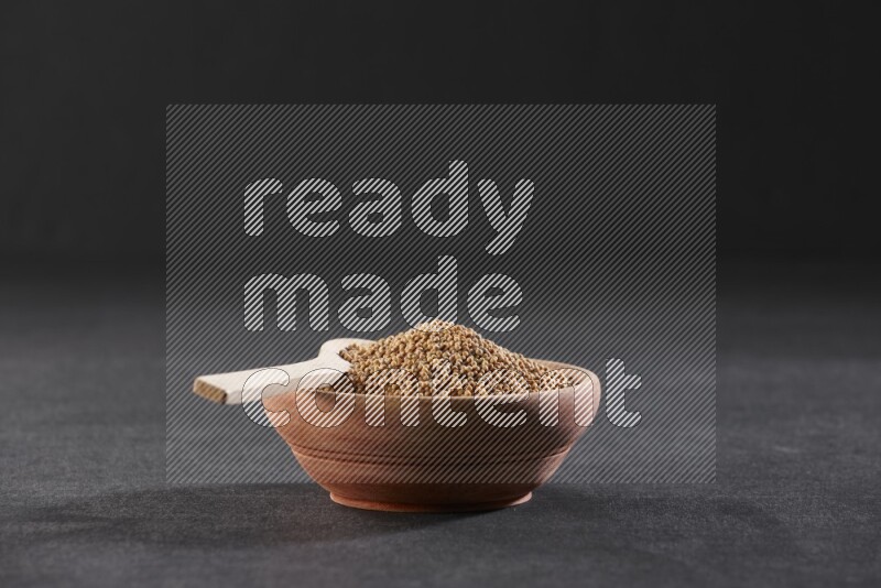 A wooden bowl and spoon full of mustard seeds on a black flooring