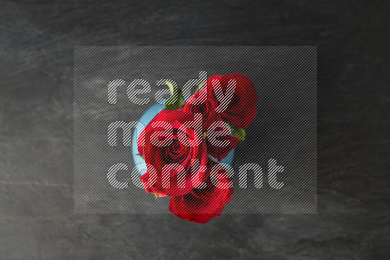 An arrangement of vivid red roses in a blue vase on black marble background