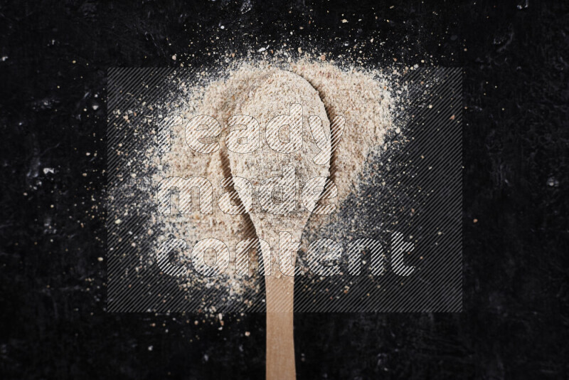 A wooden spoon full of onion powder on black background