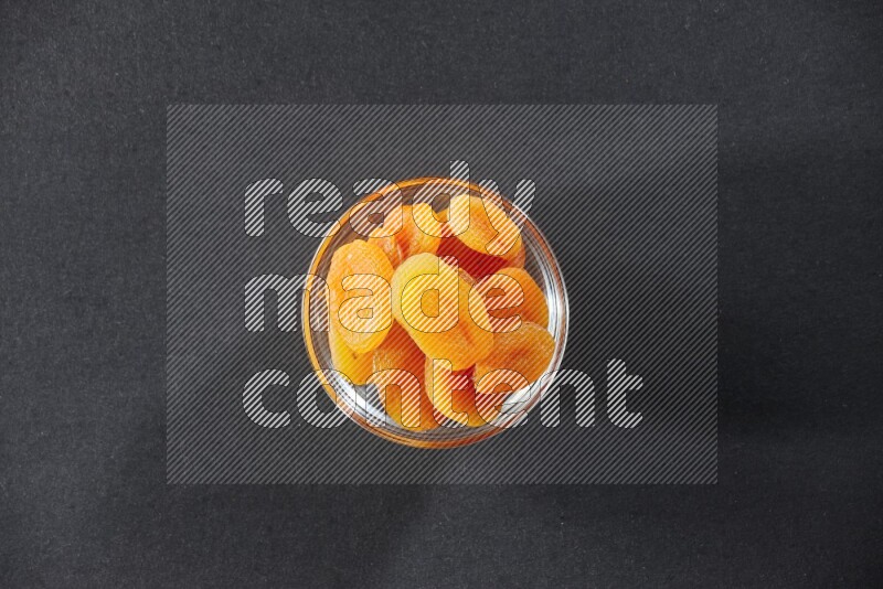 A glass bowl full of dried apricots on a black background in different angles