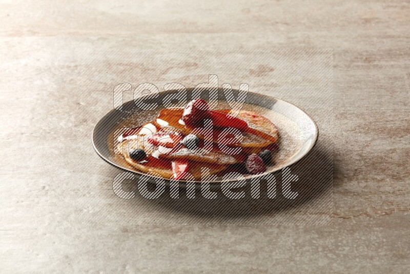 Three stacked mixed berries pancakes in a bicolor plate on beige background