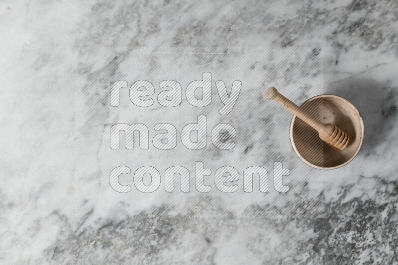 Beige pottery bowl with wooden honey dipper in it on grey marble background