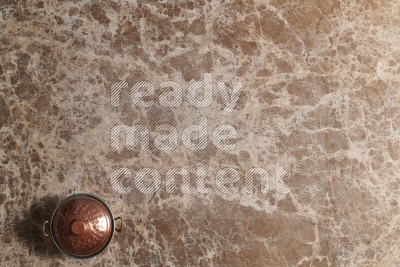 A small copper pot on beige marble background