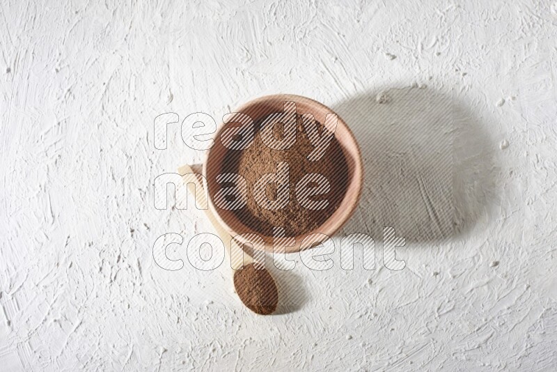 A wooden bowl and a wooden spoon full of cloves powder on a textured white flooring