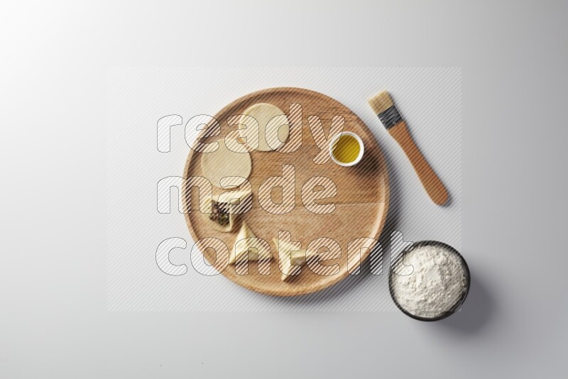 two closed sambosas and one open sambosa filled with meat while flour, and oil with oil brush aside in a wooden dish on a white background