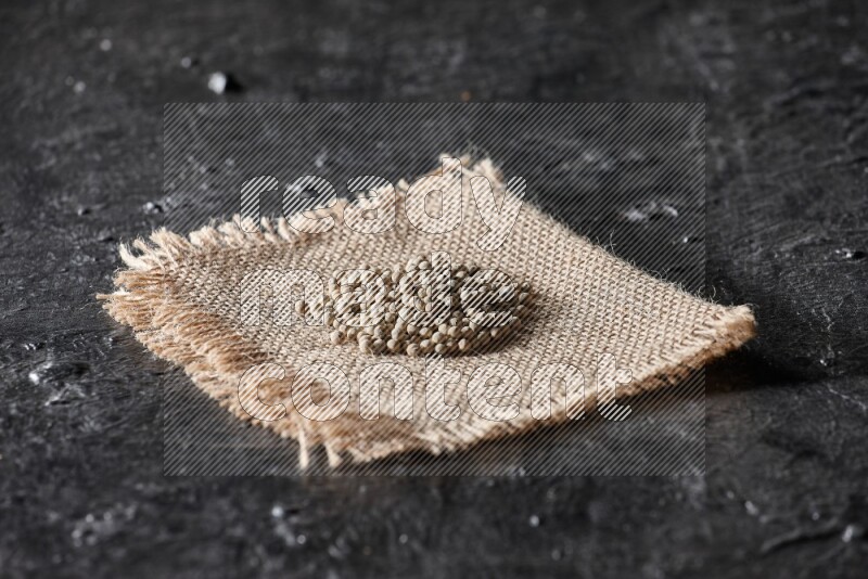 White pepper beads on a burlap piece of fabric on textured black flooring