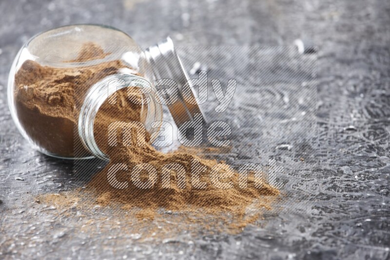 Flipped herbal glass jar full of cinnamon powder on textured black background