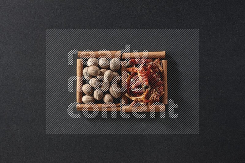 2 squares of cinnamon sticks full of nutmegs and dried red chilis on black flooring