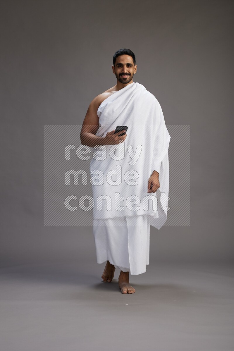 A man wearing Ehram Standing texting on phone on gray background
