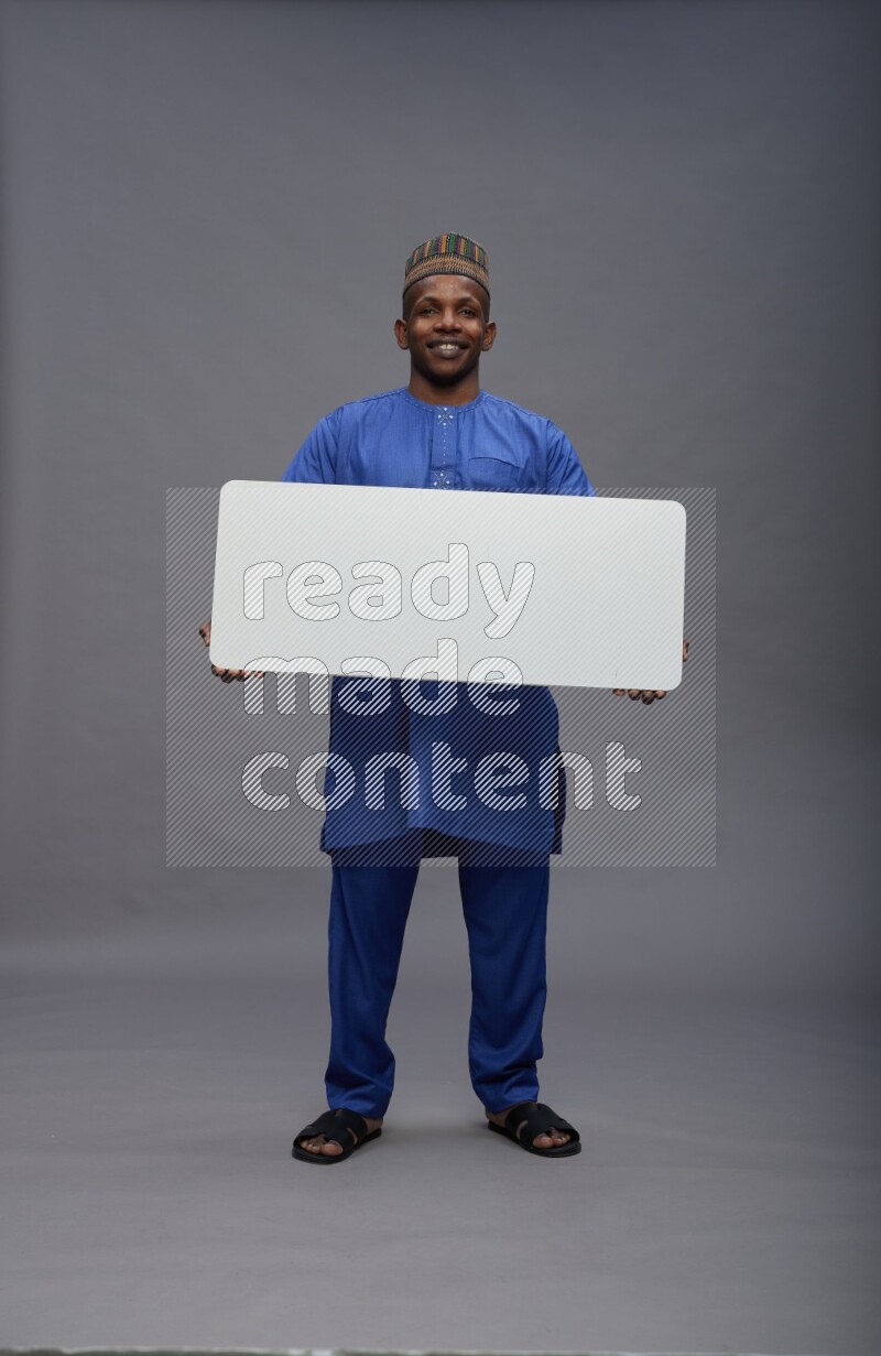 Man wearing Nigerian outfit standing holding board on gray background
