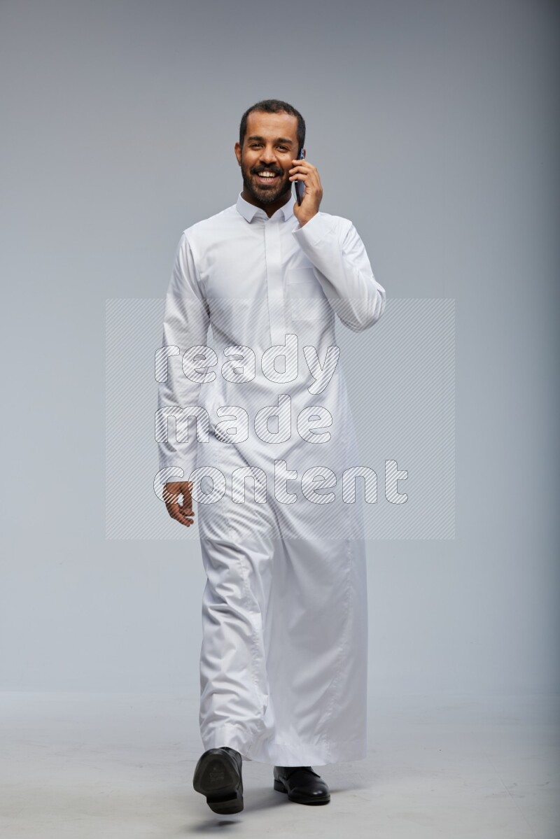 Saudi man wearing Thob standing talking on phone on Gray background