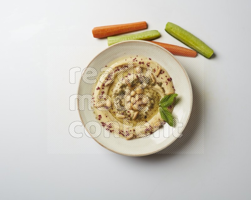 Hummus in a pottry plate garnished with zaatr & sumak on a white background