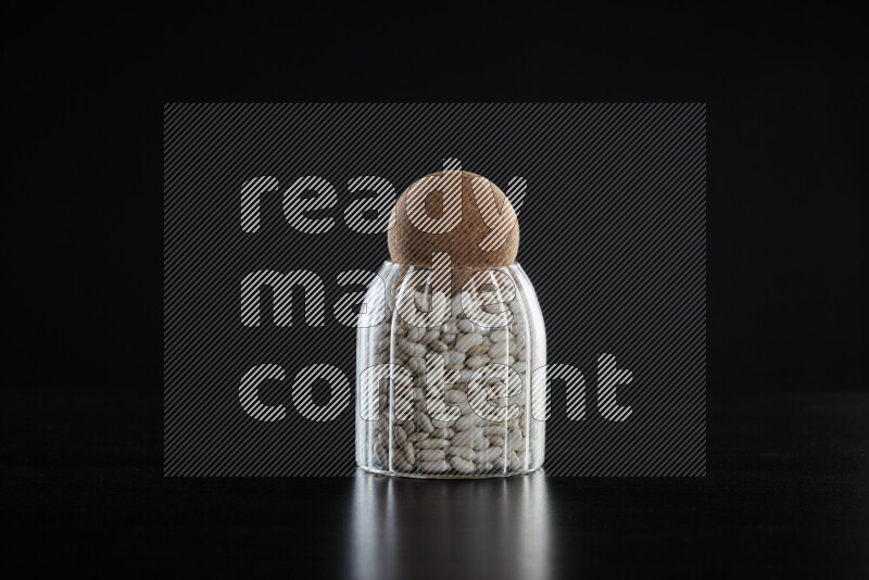 White beans in a glass jar on black background