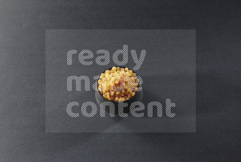 A black pottery bowl full of raisins on a black background in different angles
