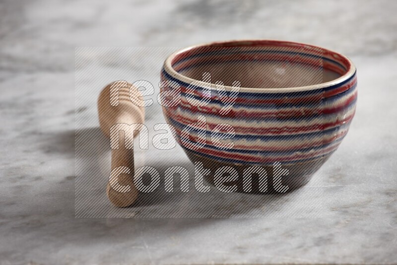 Multicolored pottery bowl with wooden honey dipper on the side on grey marble background