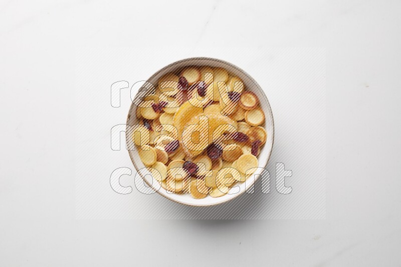 Top-view shot of orange candy cereal pancakes in a round bowl on white background