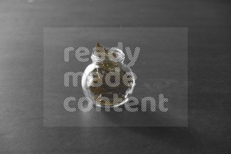 A glass spice jar full of bay laurel leaves on black flooring
