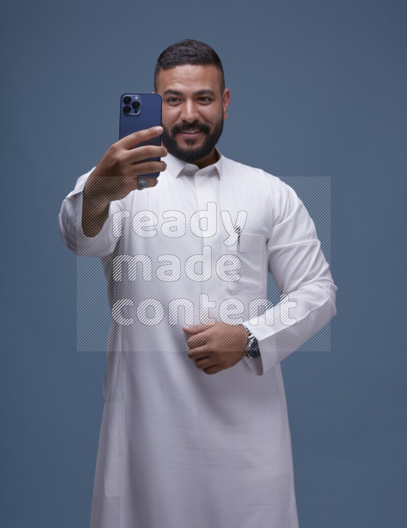 A Saudi man Taking A Selfie on Blue Background wearing Saudi Thob