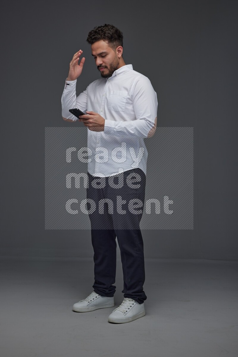 A man wearing smart casual standing and using his phone eye level on a gray background