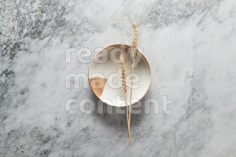 Wheat stalks on multicolored pottery plate on grey marble background